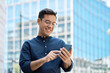 © insta_photos - Happy young Hispanic business man manager using financial banking mobile apps on cell phone standing in city, professional businessman holding smartphone in hands looking at cellphone outdoor office.