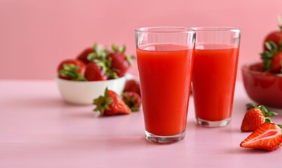 Strawberry juice in glass cup isolated on pink studio background. Next to strawberry juice are whole strawberry fruit and sliced ​​strawberry fruit. Close up view.	