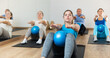 © JackF - Young girl maintaining active lifestyle exercising with small pilates ball during group class in modern fitness center, doing sit-ups for abs muscles