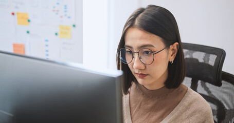 Young adult Asian female software developer coding program on desktop computer. Woman work from home, remote working, freelance programmer job, smart digital nomad lifestyle concept