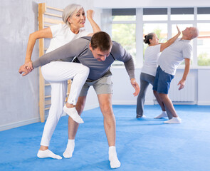 Wall Mural - Trainer and mature woman train painful hold on self-defense course in a sport gym