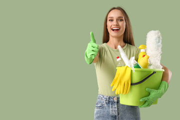 Wall Mural - Pretty young woman with cleaning supplies showing thumb-up on green background