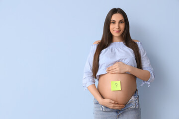 Wall Mural - Young pregnant woman and sticky paper with question mark on her belly against blue background