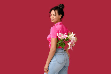 Poster - Beautiful young African-American woman with pink lily flowers on red background