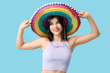 Wall Mural - Young woman in colorful sombrero dancing on blue background. Cinco de Mayo celebration