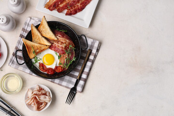 Wall Mural - Frying pan with fried egg, bacon, toasts and tomatoes on napkin on white background. Top view