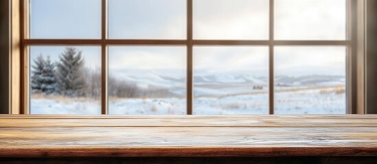 Wall Mural - Wooden table surface with product display space framed by a blurred window revealing a scenic snowy winter landscape outside