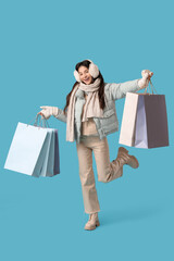 Poster - Beautiful young woman in warm clothes with shopping bags on blue background