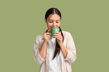 Poster - Beautiful young Asian woman drinking hot tea on green background