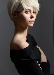 Poster - Elegant young woman with short blonde hair posing in a stylish black outfit, showcasing confidence and modern fashion aesthetics. Contemporary portrait in muted tones.