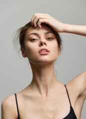 Poster - Confident young woman with tousled hair striking a pose. She wears a simple black top, showcasing natural beauty against a soft grey background.