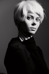 Poster - Elegant young woman with short blonde hair in black outfit, showcasing a contemplative expression against a soft gradient background. Fashion and beauty concept.