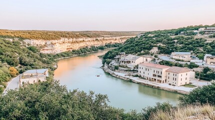 Poster - Serene river valley scene at sunset, showcasing a quaint village nestled amongst lush greenery and dramatic cliffs.