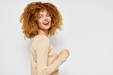 Wall Mural - Smiling woman with curly hair, wearing a beige sweater, against a light gray background, expressing happiness and joy, suitable for lifestyle and beauty concepts