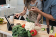 © crizzystudio - Young couple preparing a healthy meal together in a modern kitchen, following a recipe on a tablet, pointing at fresh ingredients and discussing the cooking process with joy