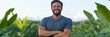 © Iryna - A man is smiling and standing in a field of green plants. Concept of happiness and contentment, as the man is enjoying his time in the natural setting