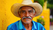 © Keopaserth - smiling elderly man wearing straw hat and blue striped shirt, sitting against vibrant yellow wall, exuding warmth and friendliness
