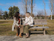 © Martí Rosselló - Blind woman sits on a park bench, smiling while talking with her friend. Her white cane rests beside her. Concept of friendship, support, and inclusion