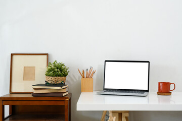 Wall Mural - Creative workspace with blank screen laptop, coffee mug and picture frame