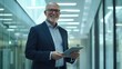 © Mohammed - Smiling senior Caucasian businessman in a suit holding a tablet in a modern office building.  Confident and successful professional.