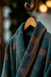 © Anastasiya - A close-up of a plaid flannel robe with green and orange checkered patterns, hanging on a wooden hook in a cozy indoor setting with soft lighting
