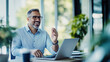 © LotusBlanc - Smiling Mature Businessman in Glasses Gesturing While Talking on Video Call at Laptop in Office, Engaged in Remote Meeting, HR Hiring Process, or Professional Team Conference in Modern Workplace.