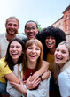 © CarlosBarquero - Vertical. Multiracial group of young students embracing and laughing together on a city street, enjoying their time together and expressing genuine happiness and friendship