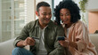 © Yuliia - Married couple family African American girlfriend and boyfriend happy man woman booking tickets with credit bank card use mobile phone buy delivery internet banking service easy money payment at home