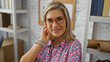 © Krakenimages.com - Woman smiling, blonde hair, wearing glasses, patterned shirt, in an office, with bookshelves, and a white brick wall, adult, female, caucasian