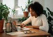© Anna - African American woman working at home desk with plants and laptop