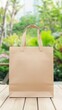 © Sergey - Mockup of a wooden paper shopping bag placed on a wooden table against a lush, green outdoor background.
