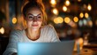 © Pinklife - A cheerful young woman is using her laptop, bathed in ambient lighting, reflecting her focus and positive energy in a beautifully arranged workspace at night.