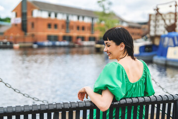 Smiling woman in green dress enjoys sunny day by waterfront in urban setting