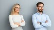 © khonkangrua - Discontent Couple Standing Apart with Crossed Arms on Gray Background in Modern Office Setting