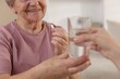 © New Africa - Caregiver giving glass of water to smiling senior woman with medical pill indoors, closeup