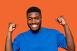 © Iryna - Man celebrates with fists raised success with joyful expression against a vibrant orange background