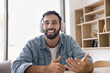 © fizkes - Young 30s Hispanic man wear headphones hold virtual meeting with client sit at desk in office, looking at camera, pass job interview or negotiates remotely, providing information, consulting on-line
