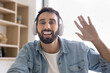 © fizkes - Webcam view, young Latin man wear wireless headphones greeting client, start videocall meeting working from home office. Online consultation, tuition, worldwide remote communication using modern tech
