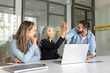 © fizkes - Mature and young teammates giving high five sit at desk with laptop, celebrate breakthrough, successfully completing project milestone, finalize important presentation or report, reach shared decision