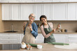 © fizkes - Joyful cooking. Two active excited females mid aged mother young adult daughter enjoy home culinary dance in aprons by kitchen table sing song by music laugh having fun taking break in baking pastries