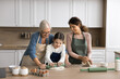 © fizkes - Family recipe. Intergenerational family older grandma young mum little child school age daughter grandkid cook at modern home kitchen together adult females teach kid knead roll dough for homemade pie