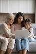 © fizkes - Online shopping. Vertical photography multi generation family of 3 happy senior mum grandmother young daughter little girl kid grandchild enjoy online web surfing on notebook order goods at ecommerce