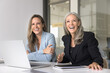 © fizkes - Joyful businesswomen having fun seated at desk with laptop, laughing seated at desk with laptop, sharing light-hearted jokes during break in their teamwork, finding humor in challenging work situation