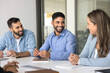 © fizkes - Young 20s Arabian staff member participate in briefing with multiethnic colleagues, sit together at desk, laughing, smiling while lead pleasant, friendly work-related conversation, Seminar event, deal