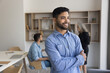 © fizkes - Young 20s professional man in business or creative field, stands in office with arms crossed, exudes sense of satisfaction, self-assurance, looks into distance with optimism. Success, personal growth