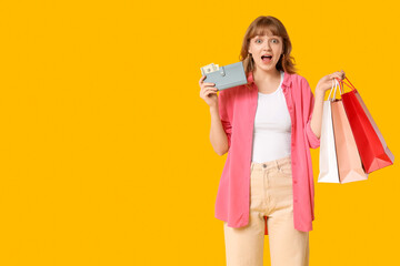 Wall Mural - Surprised young woman with wallet and shopping bags on yellow background