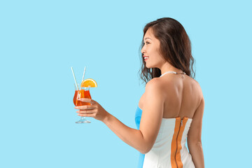 Wall Mural - Young Asian woman with aperol spritz cocktail on blue background, back view