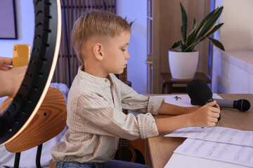 Wall Mural - Cute little boy with microphone reading music notes at home