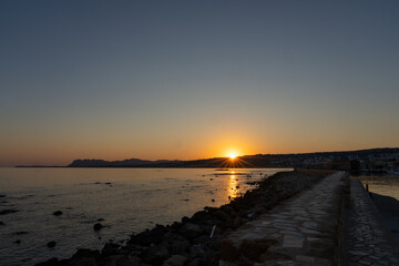 Wall Mural - Landscape in silhouette back-lit by sunrise over breakwater and harbour