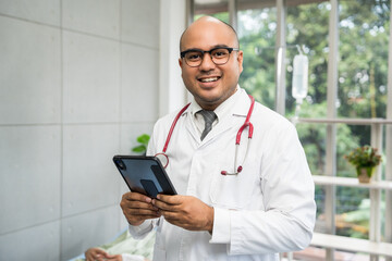 Wall Mural - Asian doctor standing posing work from hospital. Positive male physician with stethoscope in hospital background. Healthcare and medical concept.